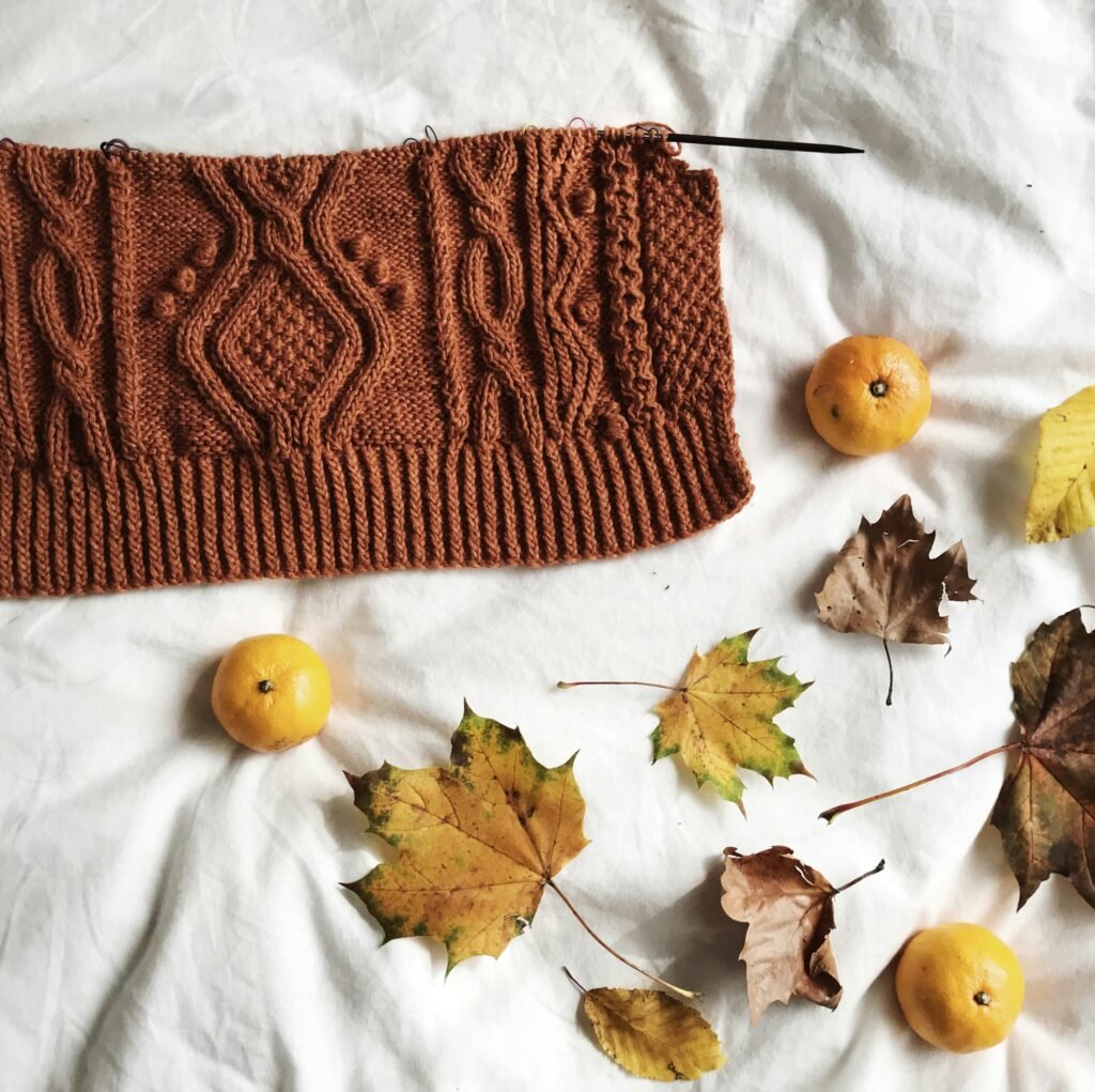 Brown knitted sweater styled with autumn leaves, an earthy fall fashion trend